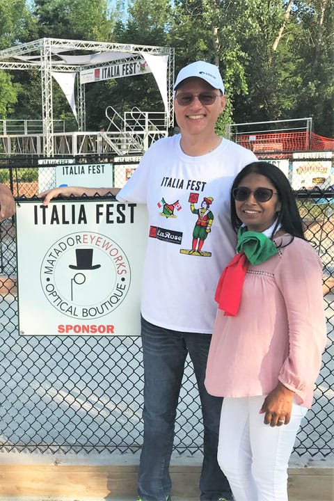 Owners of Matador Eyeworks optical boutique standing beside their sponsorship sign of Italia fest