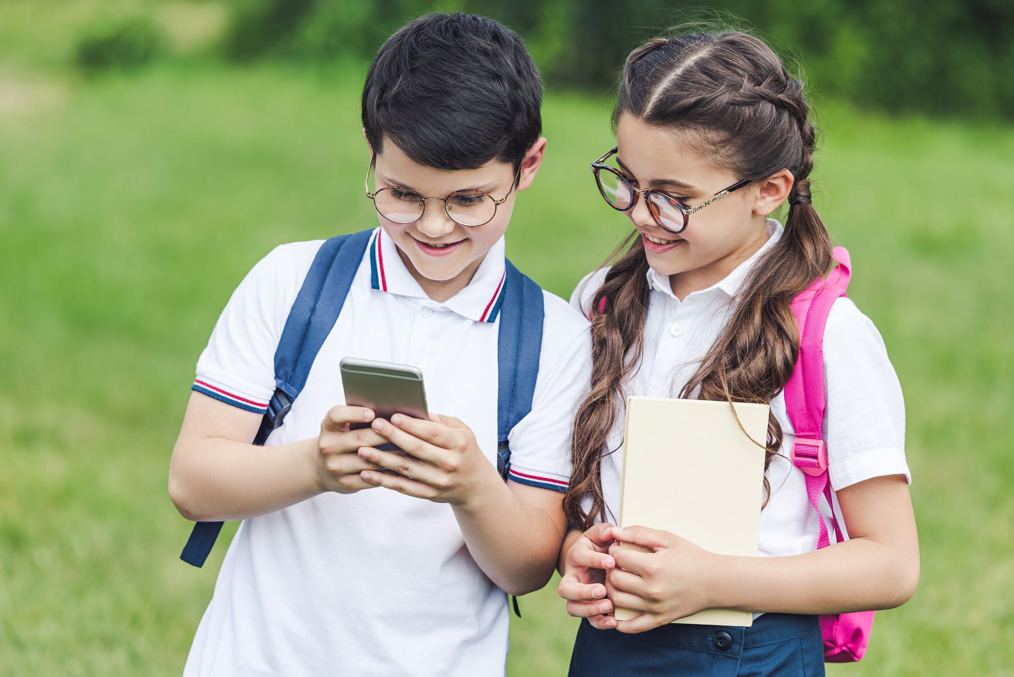 Two children wearing glasses with Zeiss Myovision myopia management lenses looking at a smart phone.