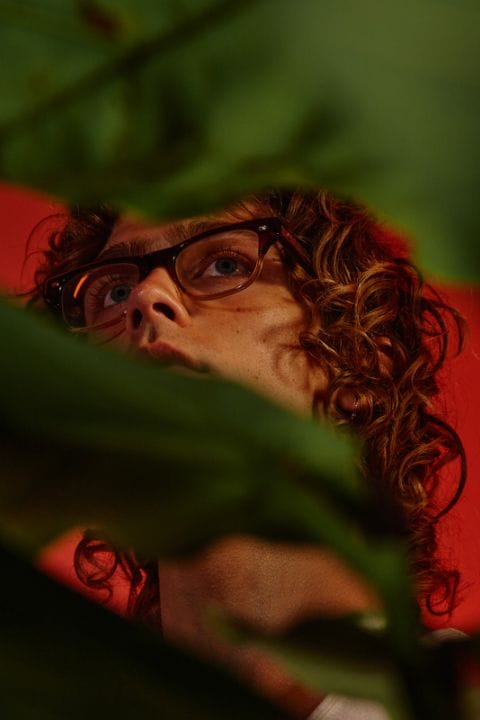 Man modelling Garrett Leight model Rodriguez behind a wide leaf plant
